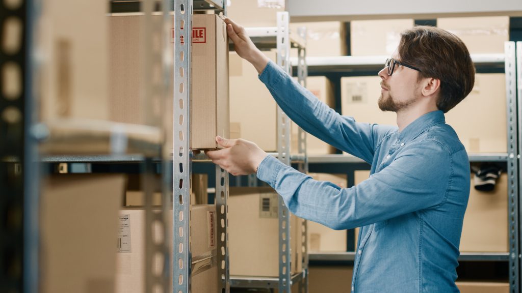 warehouse,worker,puts,cardboard,box,on,a,shelf.,in,the