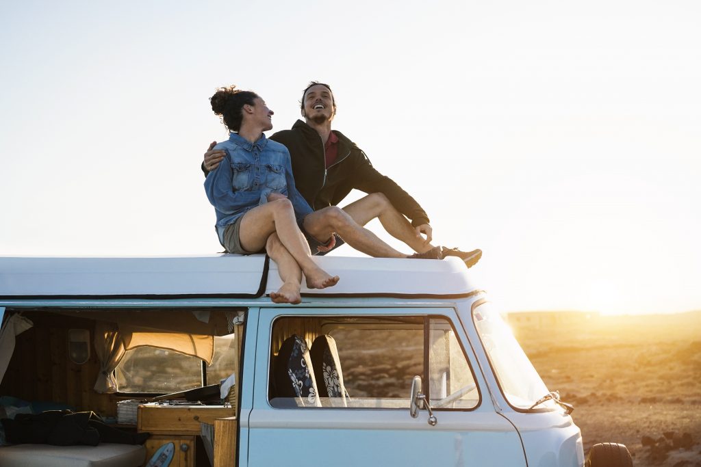 happy,couple,sitting,on,top,of,minivan,roof,at,sunset