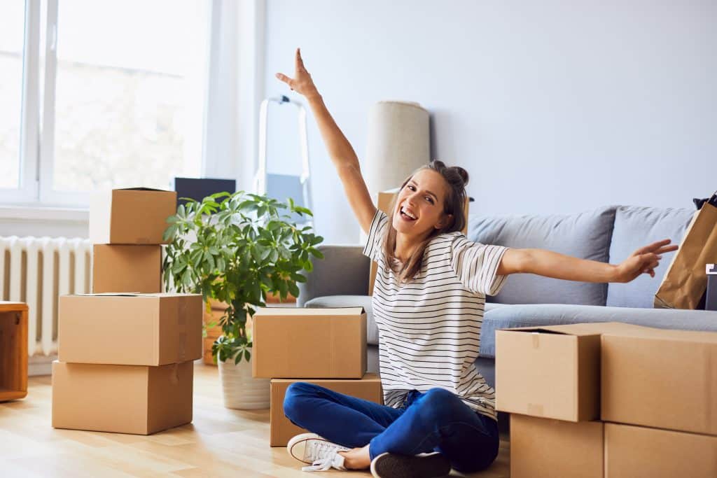 young,woman,sitting,in,new,apartment,and,raising,arms,in