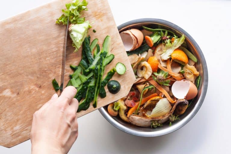 vegetable,peels,are,thrown,from,cutting,board,into,an,iron