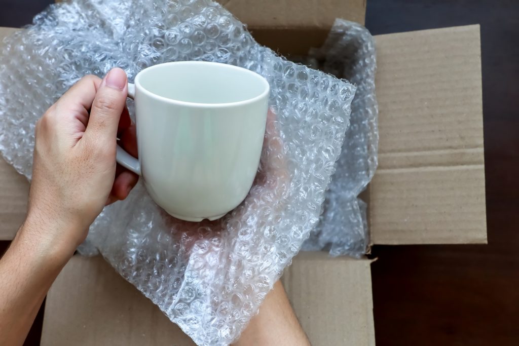 hands,holding,a,white,ceramic,cup,and,bubble,plastic,wrap,