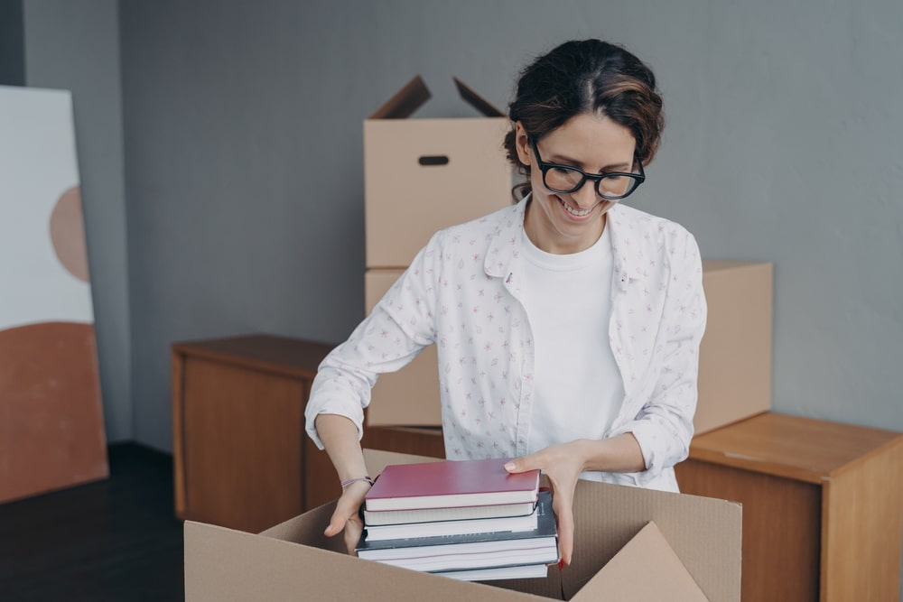young,european,woman,packing,carton,container,and,puts,textbooks,into.